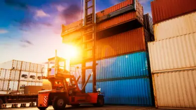 Άνοιγμα κοντέινερ σε τελωνειακό χώρο με φορτωτή και στοιβαγμένα εμπορευματοκιβώτια