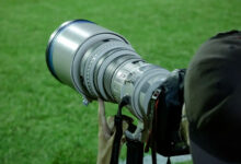 Φωτογράφος κρατά επαγγελματική κάμερα σε αθλητική φωτογράφιση, με έμφαση στον φακό