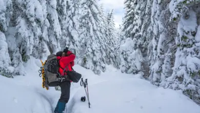 Φωτογράφος σε χιονισμένο τοπίο δουλεύει με κάμερα, φορώντας γάντια και χειμερινό μπουφάν.