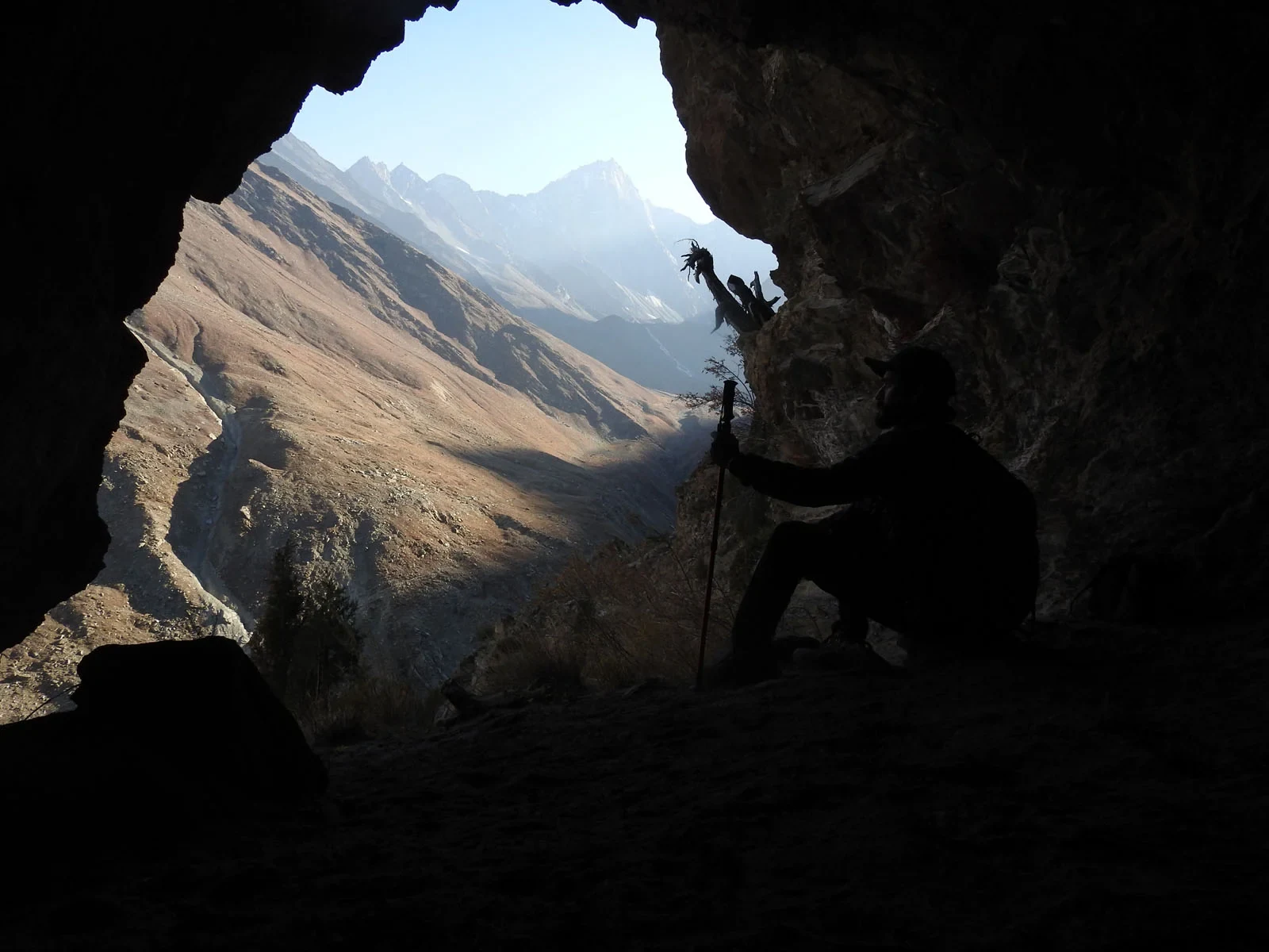 A researcher’s silhouette stands at a cave entrance overlooking a mountain valley in the western Himalayas.