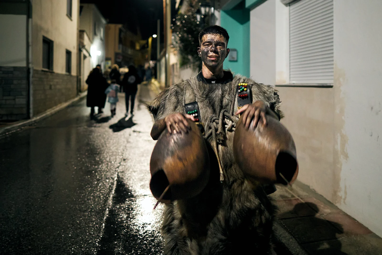 Costumed participant wearing animal skins and large bells in a Petrousa street at night