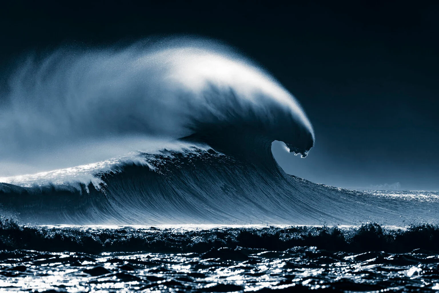 A large blue wave breaks off Tahiti as sunlight illuminates the spray.
