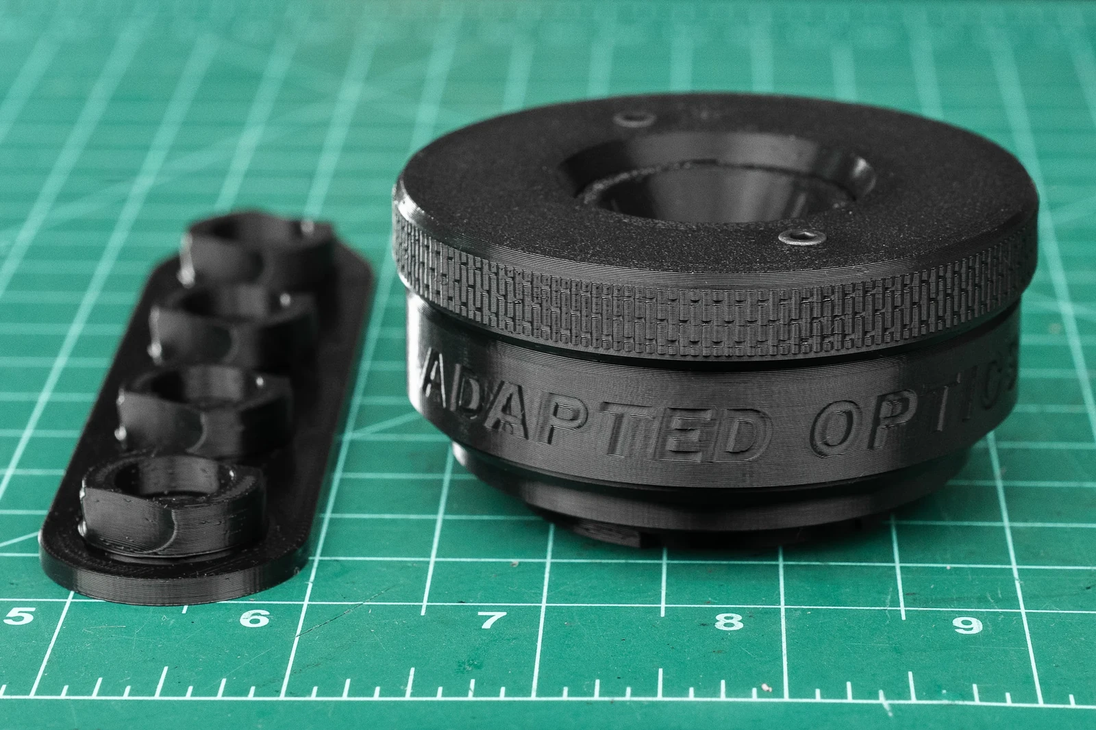 Ο μαύρος Adapted Optics Everyday Lens δίπλα στον φορέα των εναλλάξιμων διαφραγμάτων