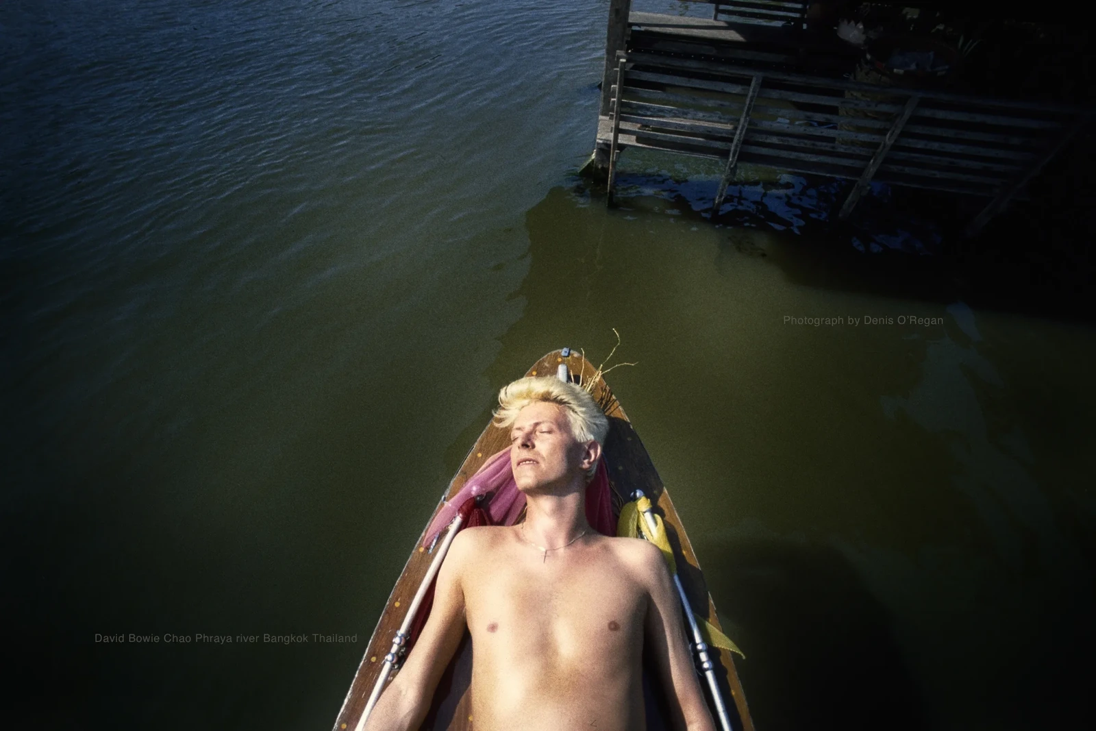 David Bowie resting in the bow of a wooden boat on the Chao Phraya river in 1983