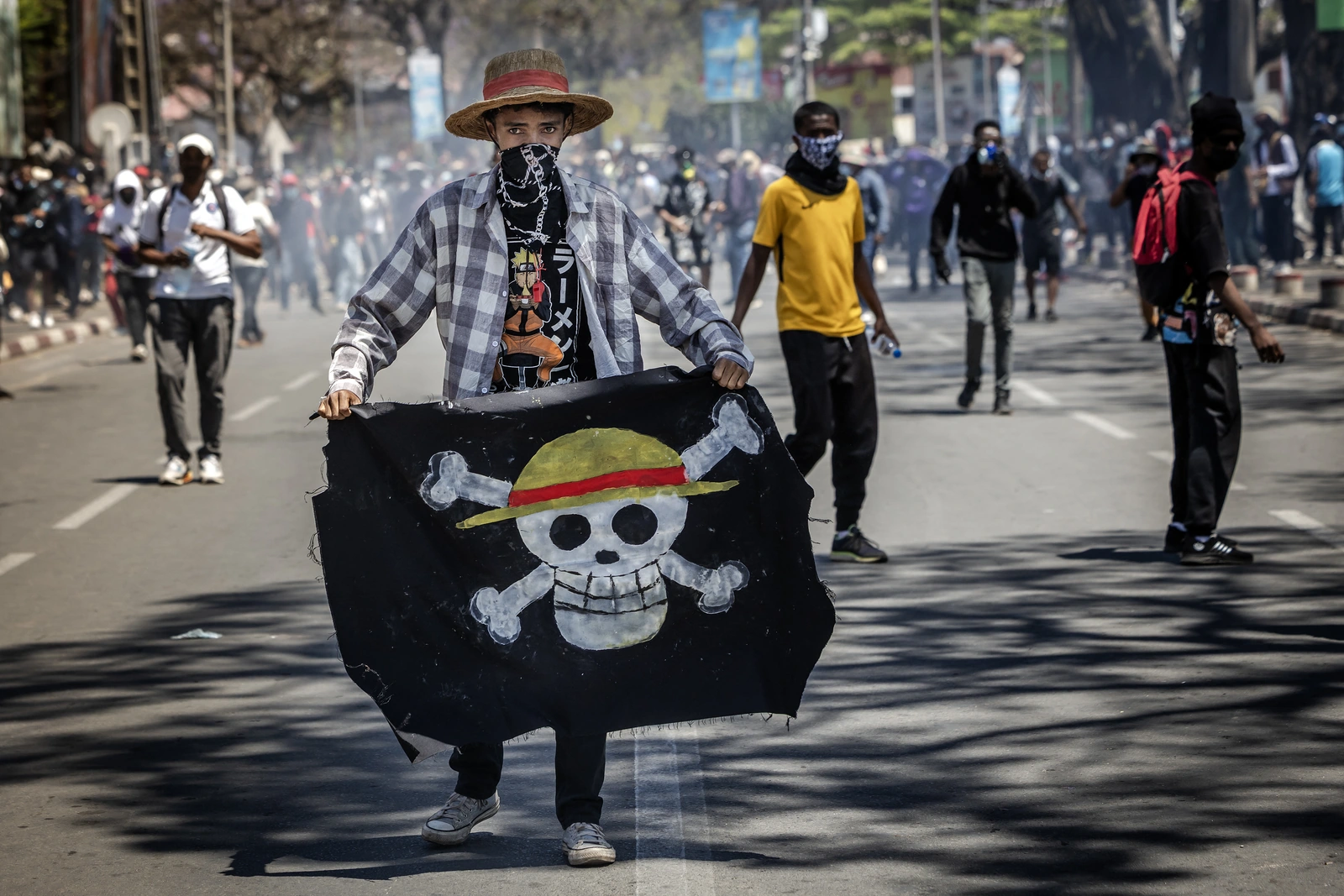 Διαδηλωτής με ψάθινο καπέλο και σημαία του One Piece μπροστά σε πλήθος στο Ανταναναρίβο