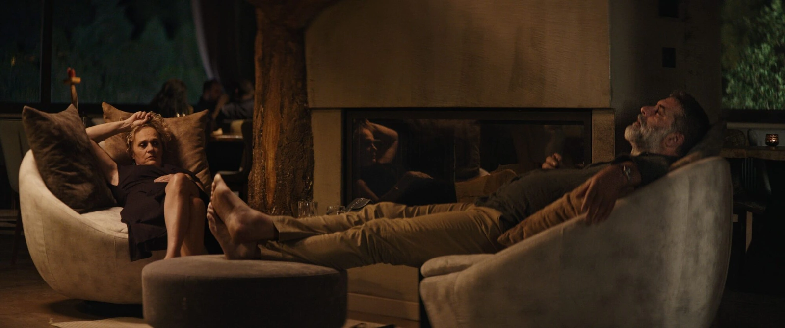 Two people in armchairs on either side of a fireplace at night