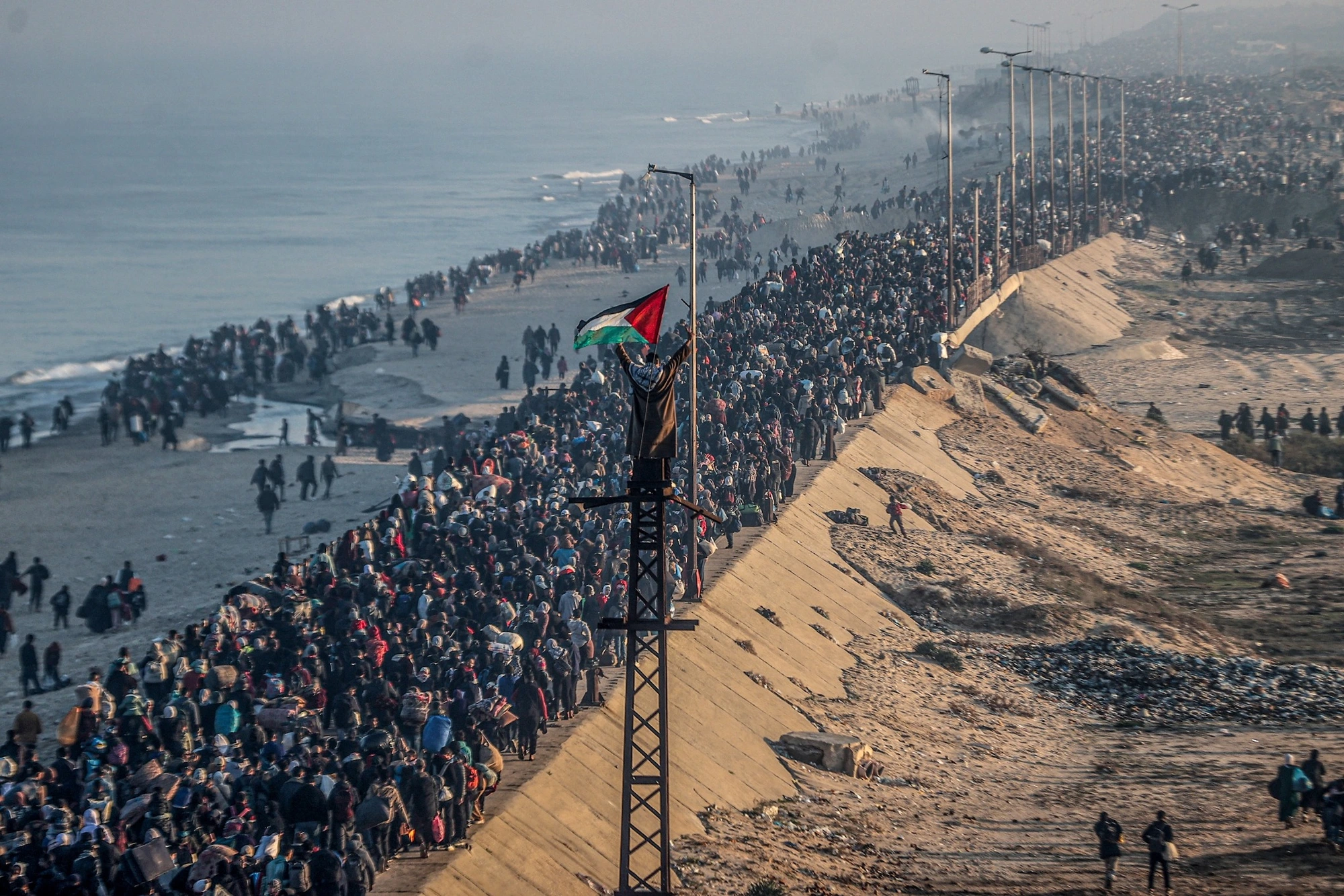 A crowd along the coast in Gaza, with a Palestinian flag in the foreground