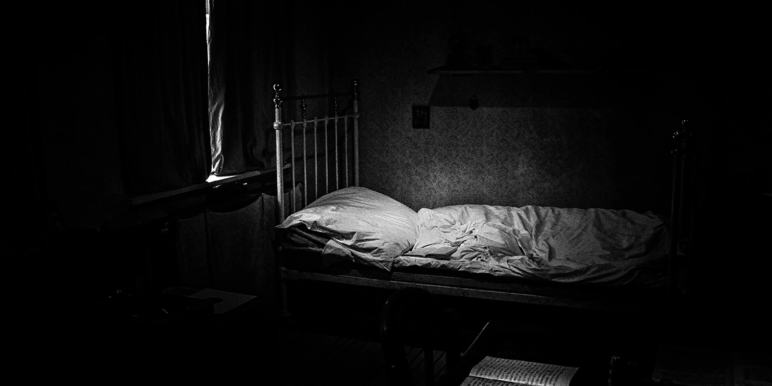 Black-and-white photograph of a bed in a dark room, from TEREN ZIELONY