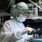 Εργαζόμενη στο εργοστάσιο Fujifilm ελέγχει φακό φορώντας προστατευτική στολή και γάντια