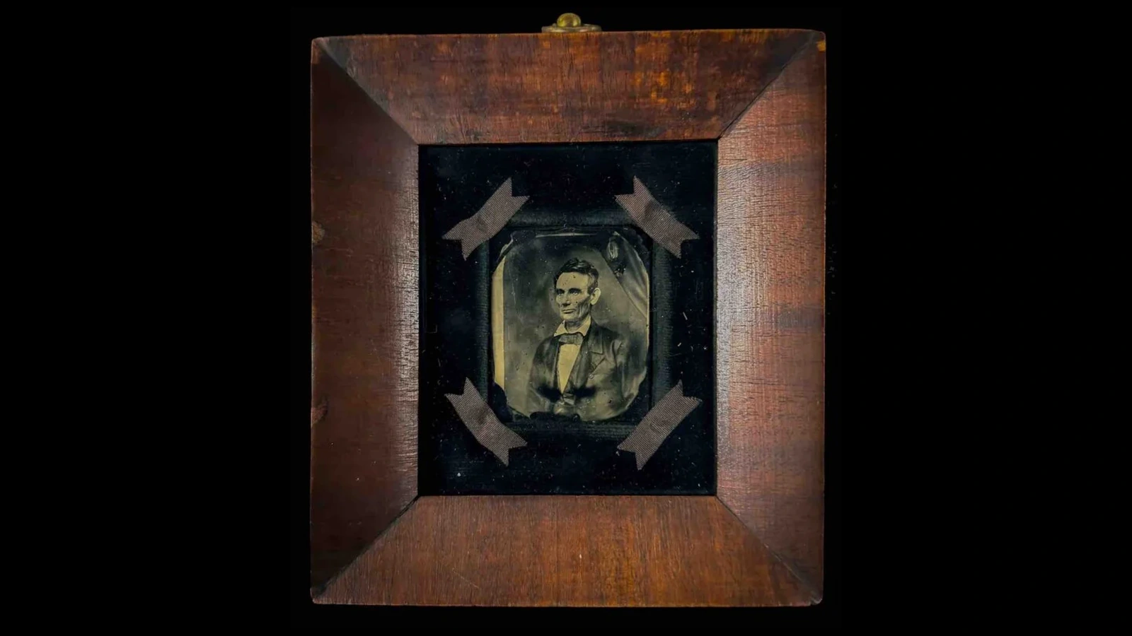 A beardless Abraham Lincoln pictured on a glass plate inside a wooden frame.