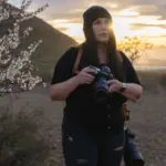 Φωτογράφος με Nikon φωτογραφική μηχανή και τηλεφακό σε εξωτερικό τοπίο κατά το ηλιοβασίλεμα