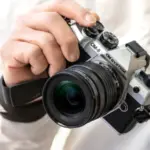 Χέρι κρατά ασημί OM SYSTEM OM-5 Mark II με φακό, σε κοντινό πλάνο
