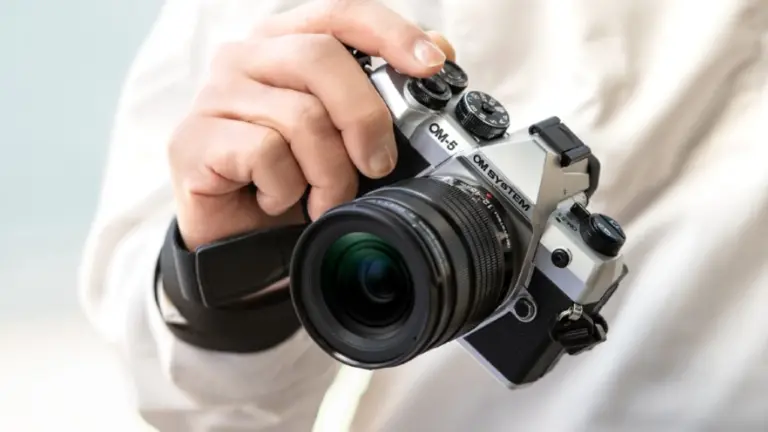 Χέρι κρατά ασημί OM SYSTEM OM-5 Mark II με φακό, σε κοντινό πλάνο