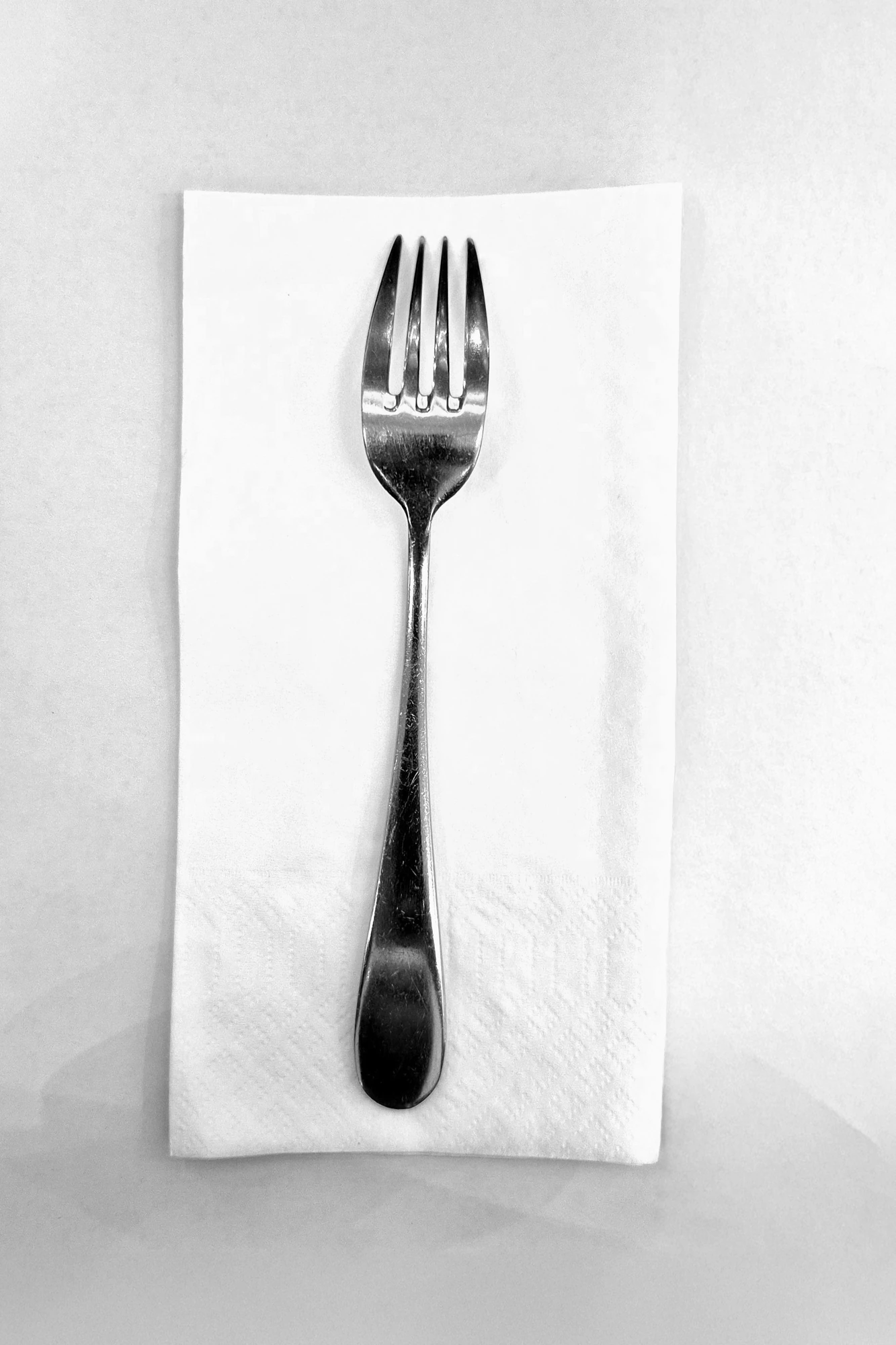 Black and white photograph of a fork on a folded white napkin