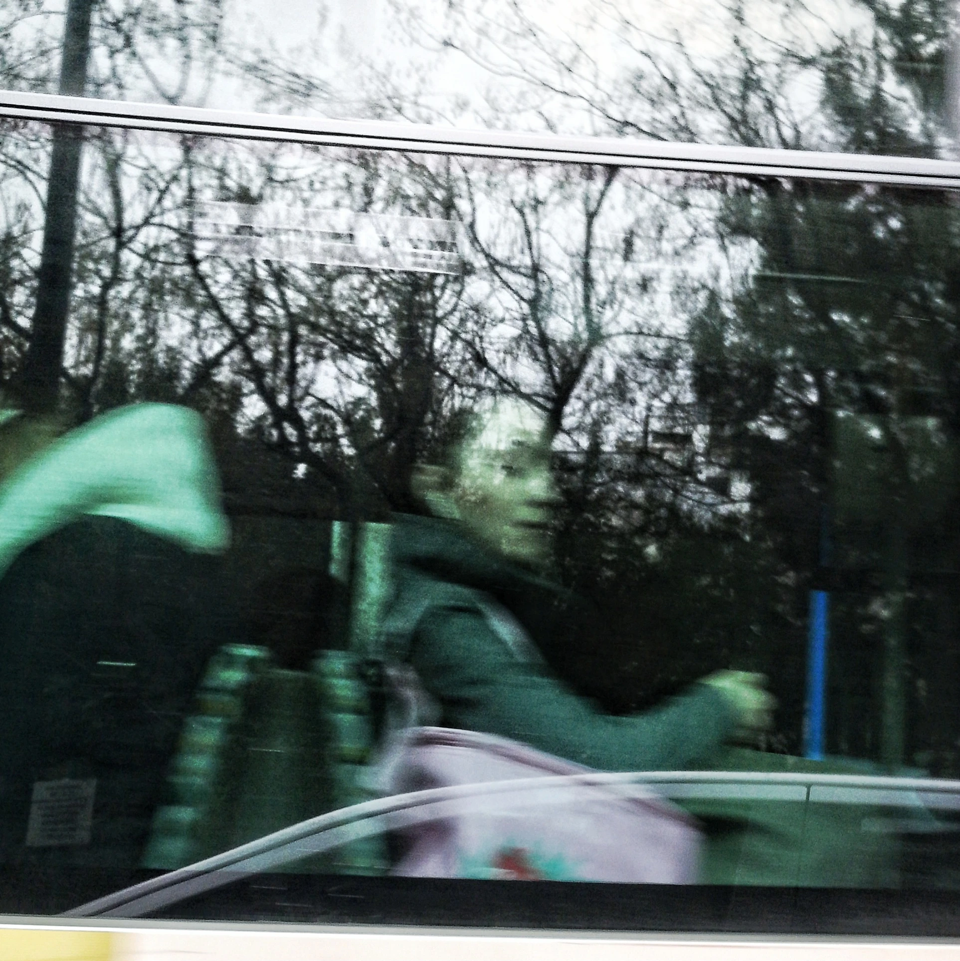 Reflections of trees and passers-by in glass with blurred green figures
