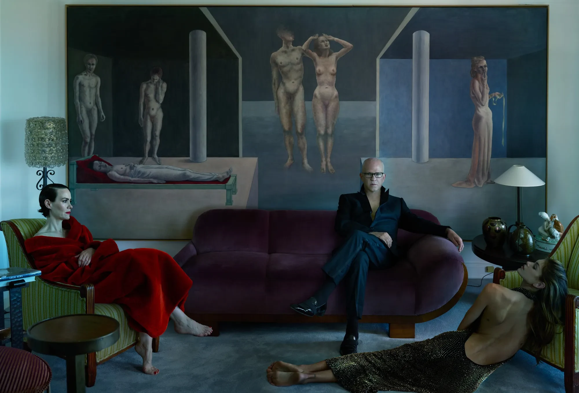 Ο Ryan Murphy καθισμένος ανάμεσα στη Sarah Paulson με κόκκινο φόρεμα και την Kaia Gerber με μαύρο, μπροστά σε μεγάλο πίνακα.