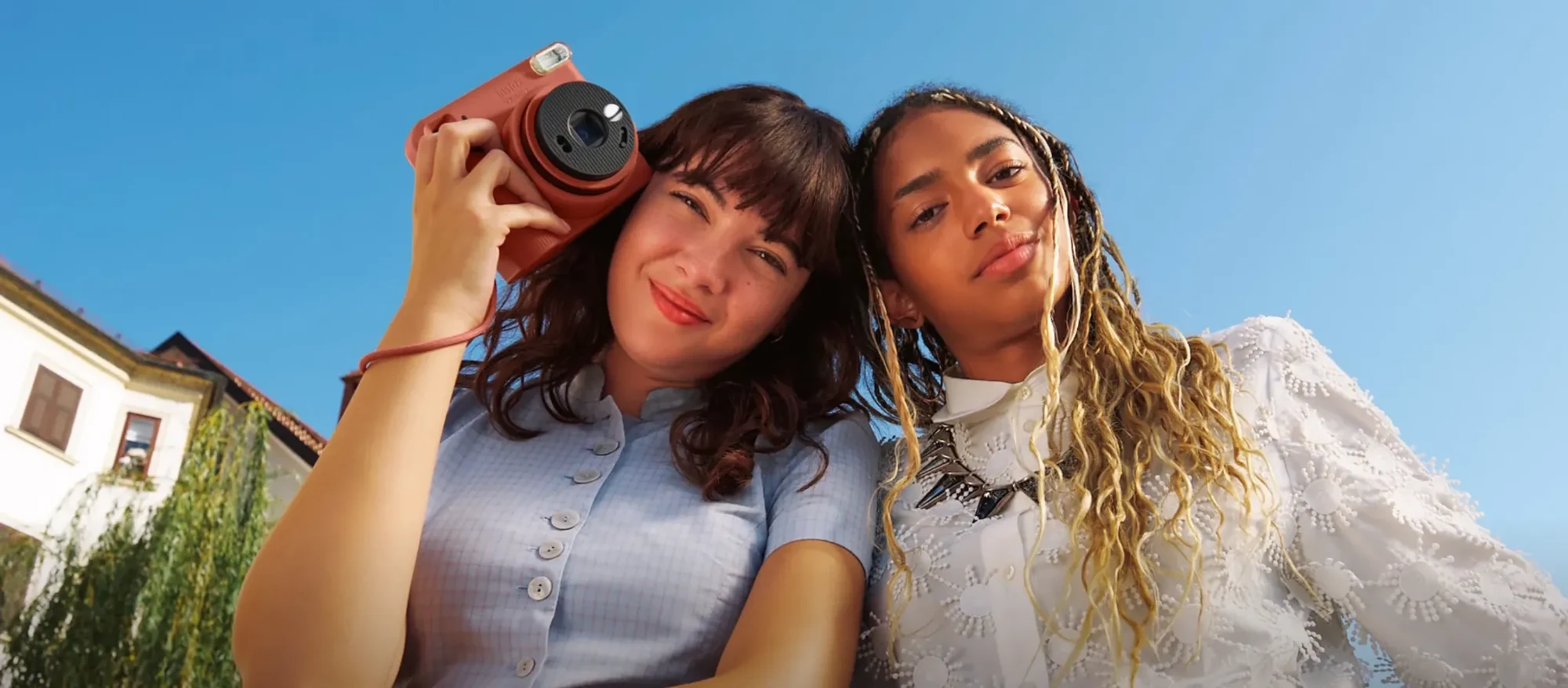 Δύο φίλες με κόκκινη instax SQUARE 2 σε εξωτερικό χώρο