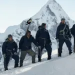 Ορειβατική ομάδα σε παγωμένη πλαγιά με φόντο ορεινή κορυφή σε σκηνή του Tenzing